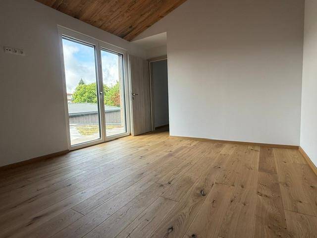 Lichtdurchfluteter Raum mit Holzboden, schräger Holzdecke und großem Zugang zur Terrasse.