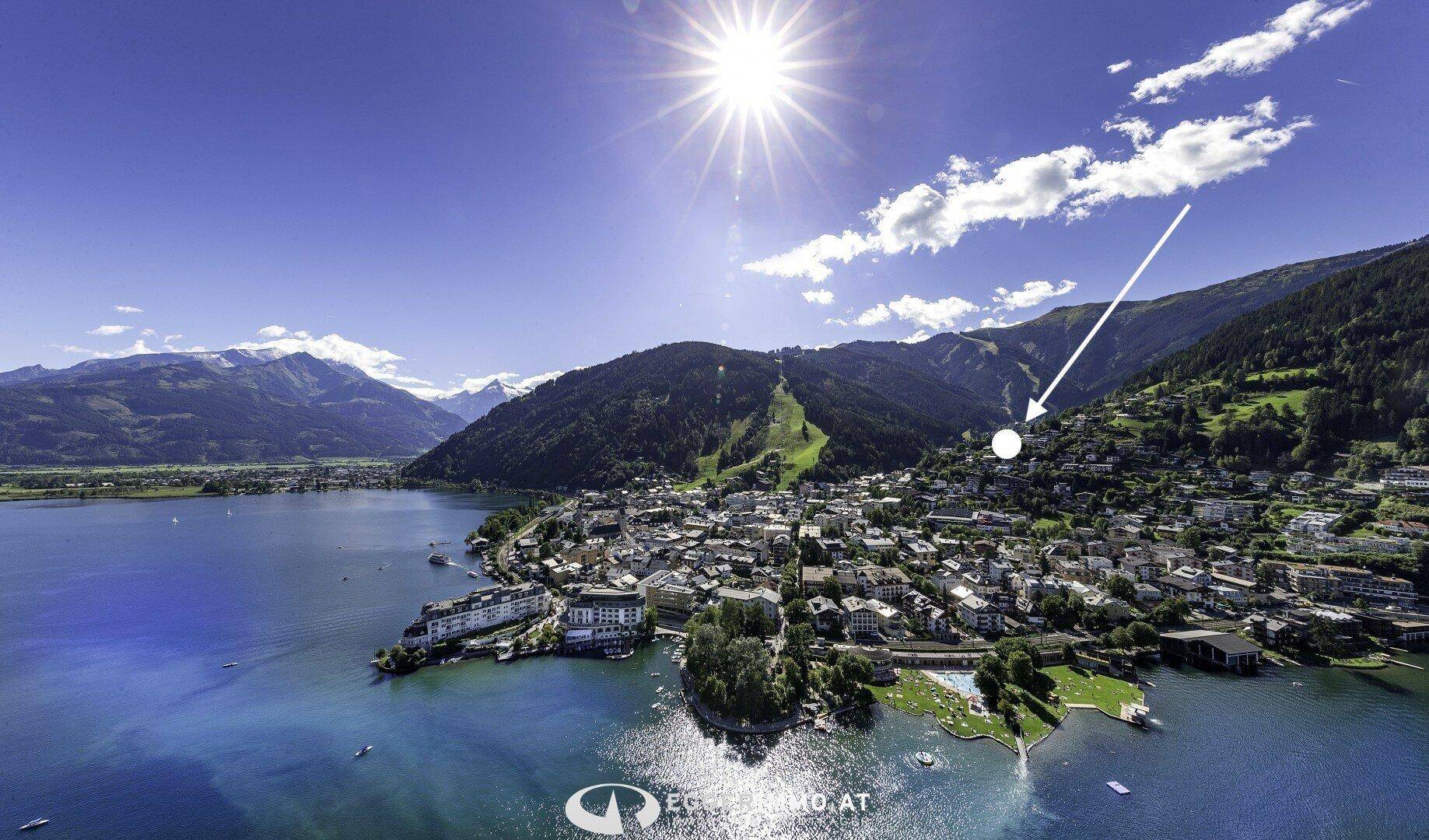 Panoramablick auf die Stadt am See, umgeben von majestätischen Bergen unter strahlendem Sonnenschein.