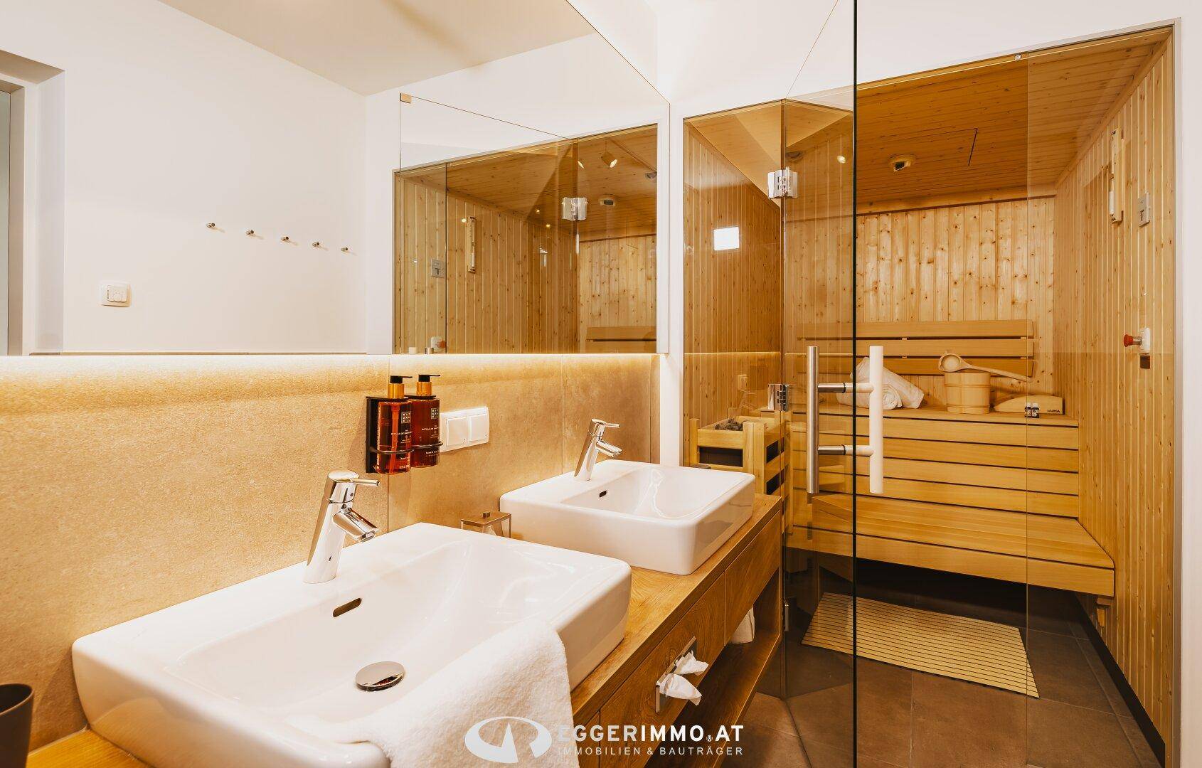 Modernes Badezimmer mit Doppelwaschbecken, großem Spiegel und einer integrierten Holzsauna.