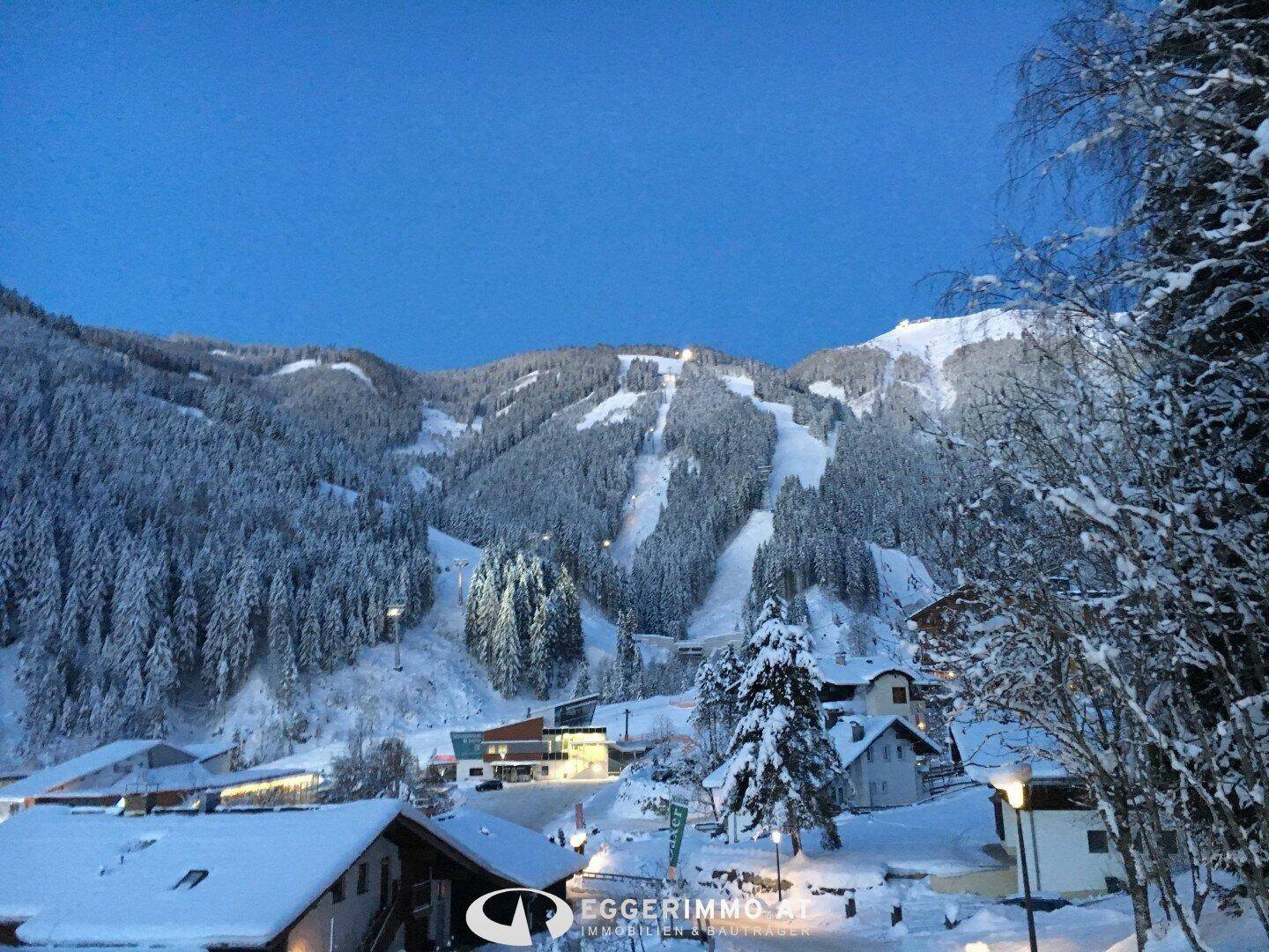 Winterlandschaft mit verschneiten Bergen und Häusern, ideal für Wintersportliebhaber.