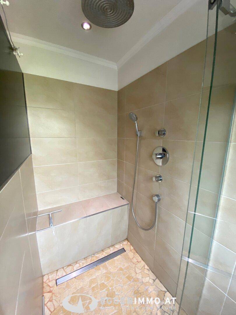 Moderne begehbare Dusche mit Fliesen, Glasabtrennung und Regenduschkopf.
