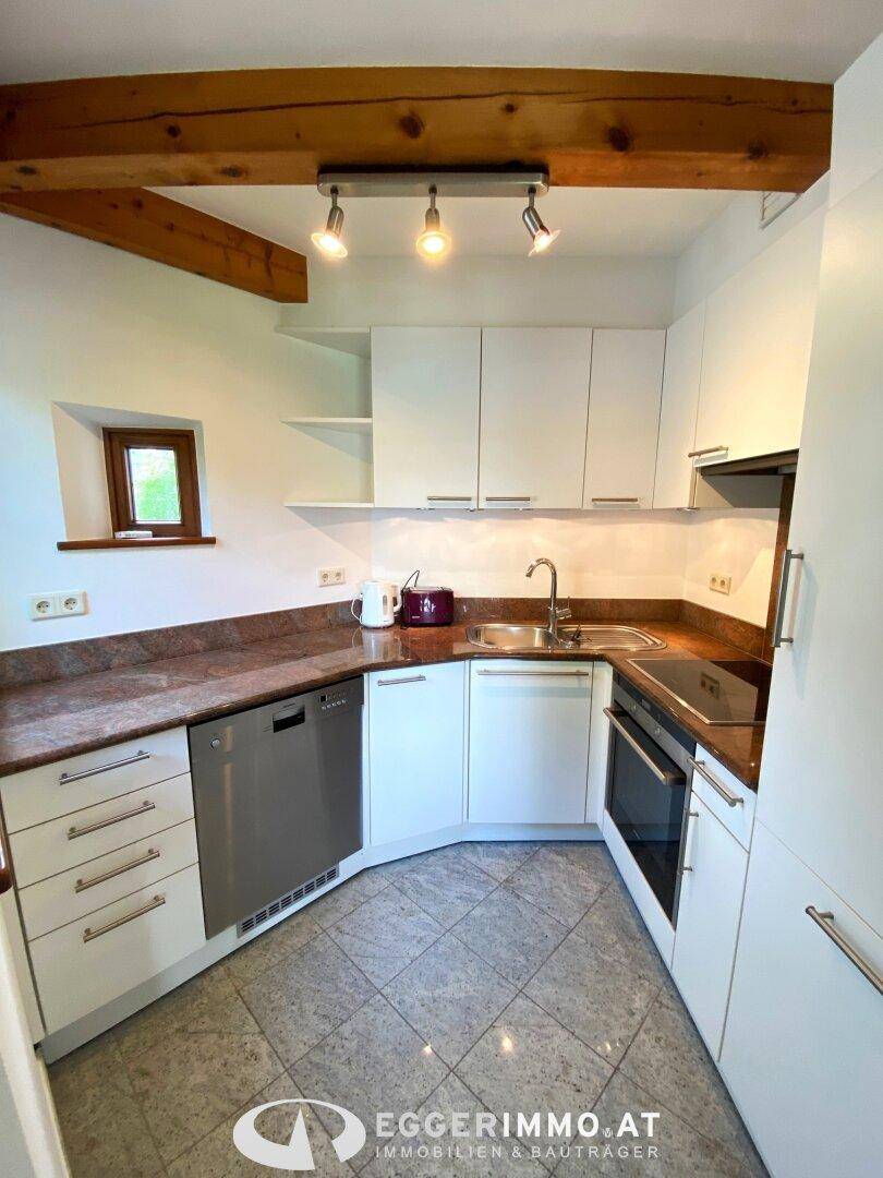 Helle Küche mit weißen Fronten, Granitarbeitsplatte und Holzbalken an der Decke.