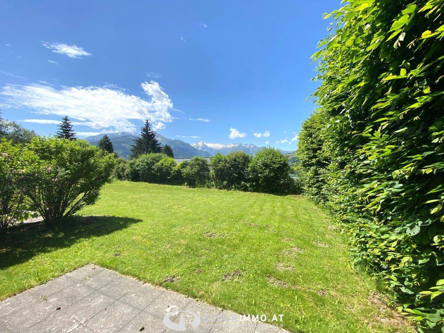Weitläufiger Garten mit Rasenfläche, Terrasse und Blick auf die umliegende Berglandschaft.