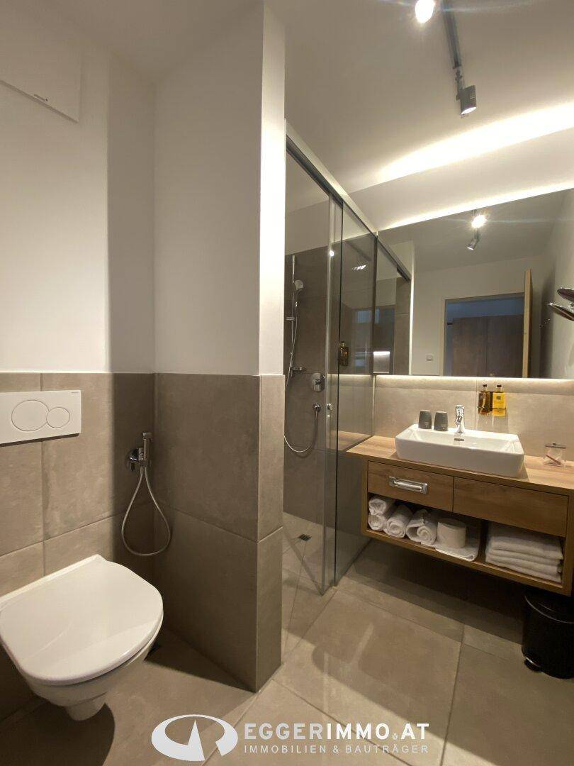 Zeitgemäßes Badezimmer mit wandhängendem WC, begehbarer Dusche und eleganten Fliesen.