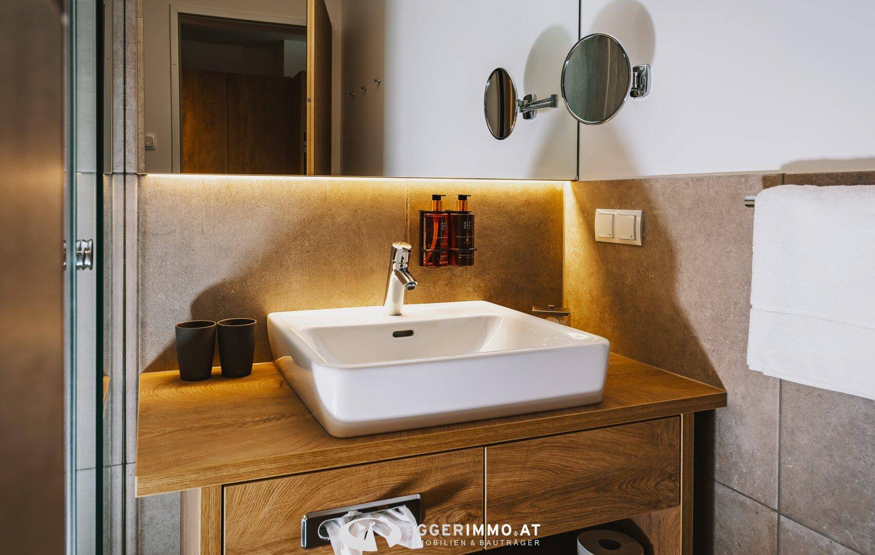 Modernes Badezimmer mit stilvollem Aufsatzwaschbecken, Holzunterschrank und beleuchtetem Spiegel.