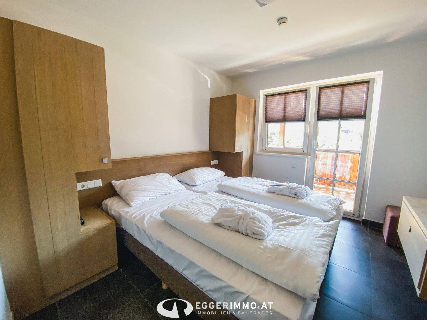 Helles Schlafzimmer mit zwei Einzelbetten, Holzmöbeln und Fenster mit Zugang zum Balkon.