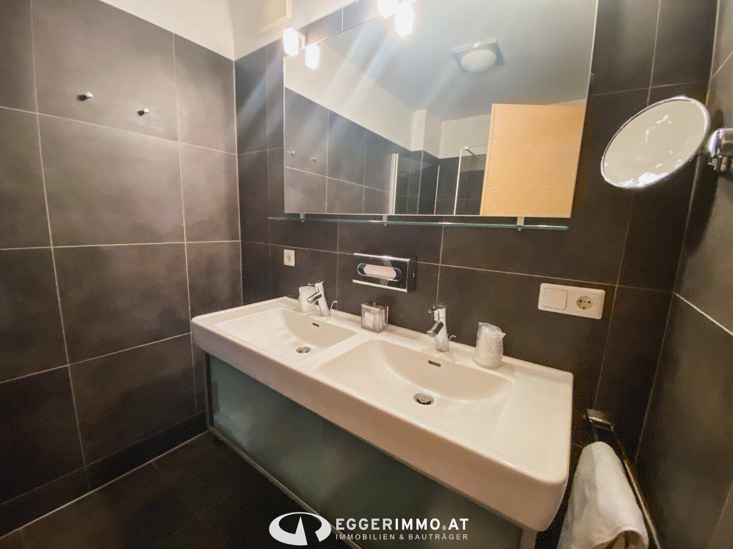 Modernes Badezimmer mit Doppelwaschbecken und großen dunklen Fliesen an Wänden und Boden.