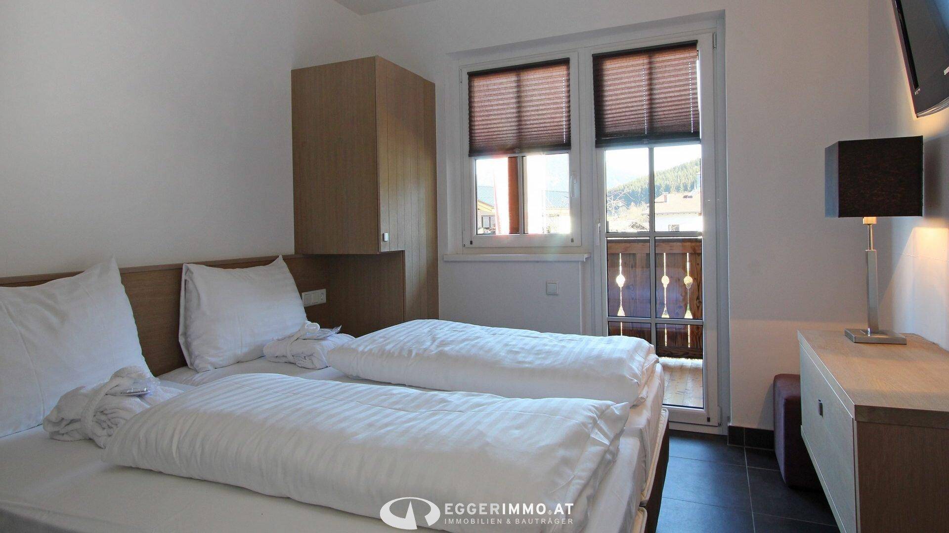Gemütliches Schlafzimmer mit zwei Einzelbetten, Nachttischlampe und Fenster mit Blick nach draußen.