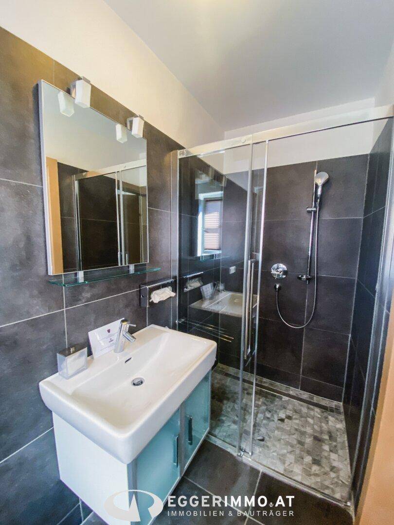 Modernes Badezimmer mit dunklen Fliesen, Duschkabine und Waschtisch mit Unterschrank.