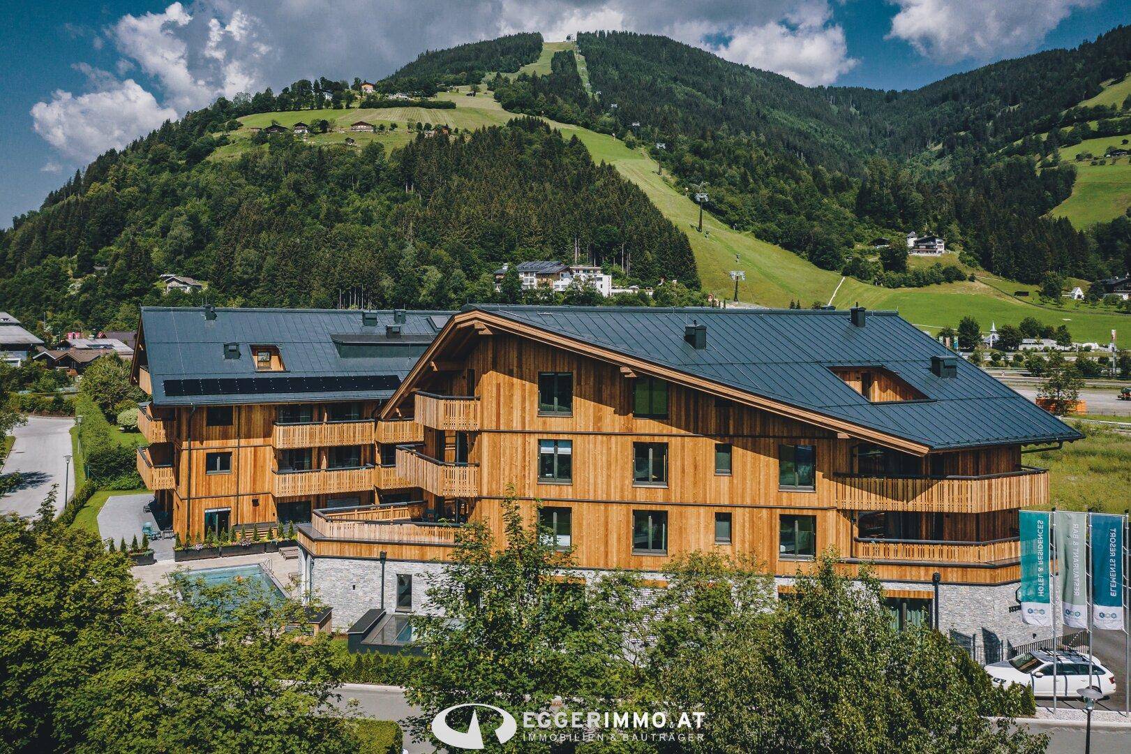 Attraktives Holzgebäude in alpiner Umgebung mit Blick auf die Skipiste und grüne Hügel.