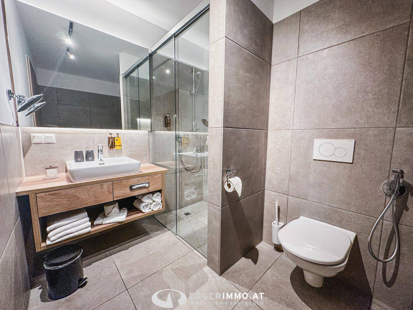 Modernes Badezimmer mit großformatigen Fliesen, Waschtisch und einer geräumigen begehbaren Dusche.