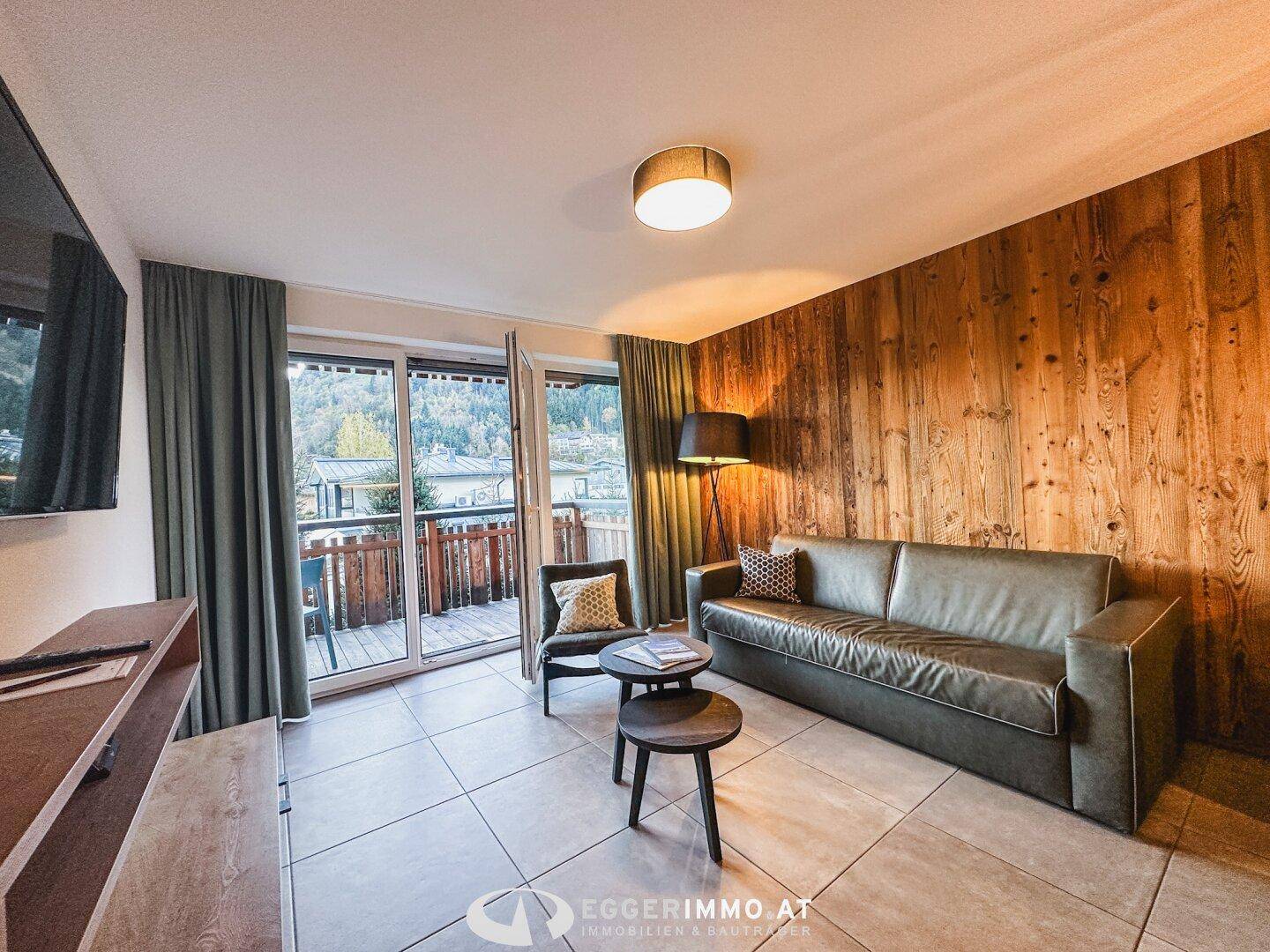 Gemütliches Wohnzimmer mit Holzwand, bequemer Couch und Zugang zu einem Balkon mit Bergblick.