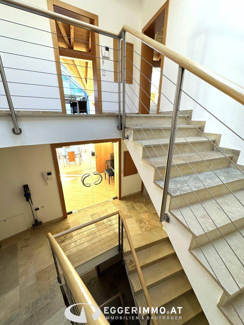Offene Treppe mit Steinplatten und modernen Geländern, die verschiedene Wohnbereiche verbindet.
