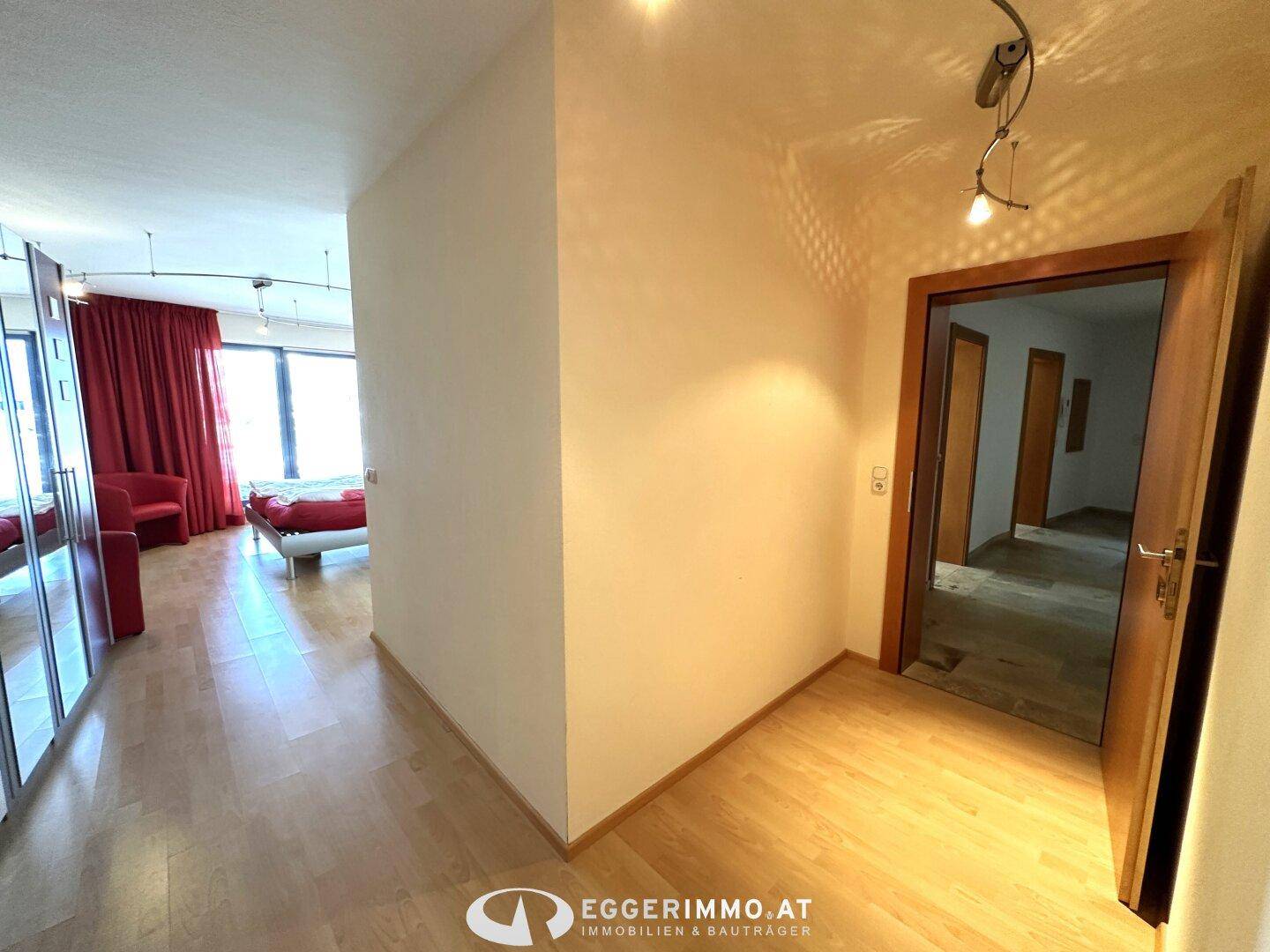 Flur mit Holzboden und Spiegelschränken, der zu einem Schlafzimmer mit roten Vorhängen führt.