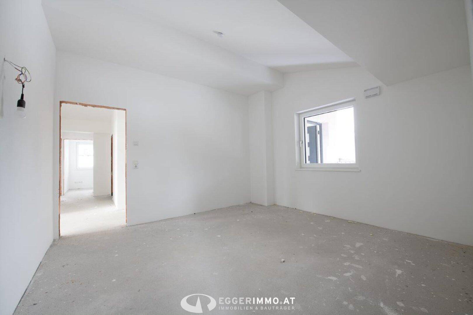 Helles, unfertiges Zimmer mit weißen Wänden und einem Fenster, das Tageslicht hereinlässt.