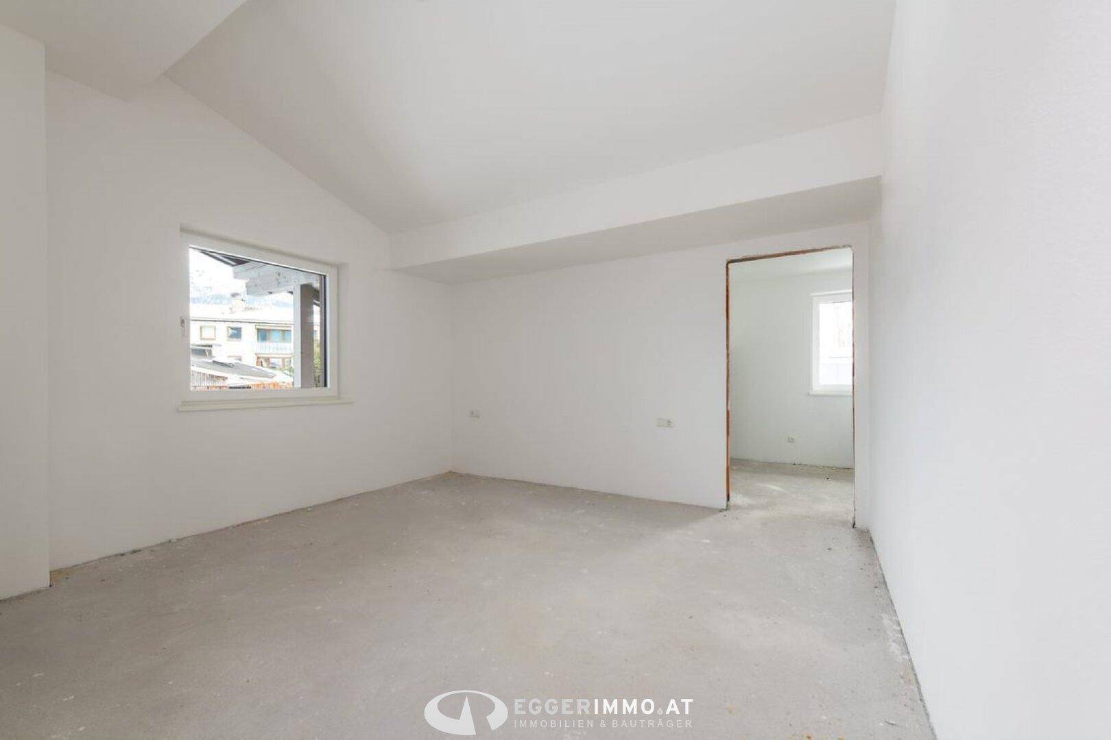Unfertiges Zimmer mit weißen Wänden und einem Fenster, bereit für den Innenausbau.