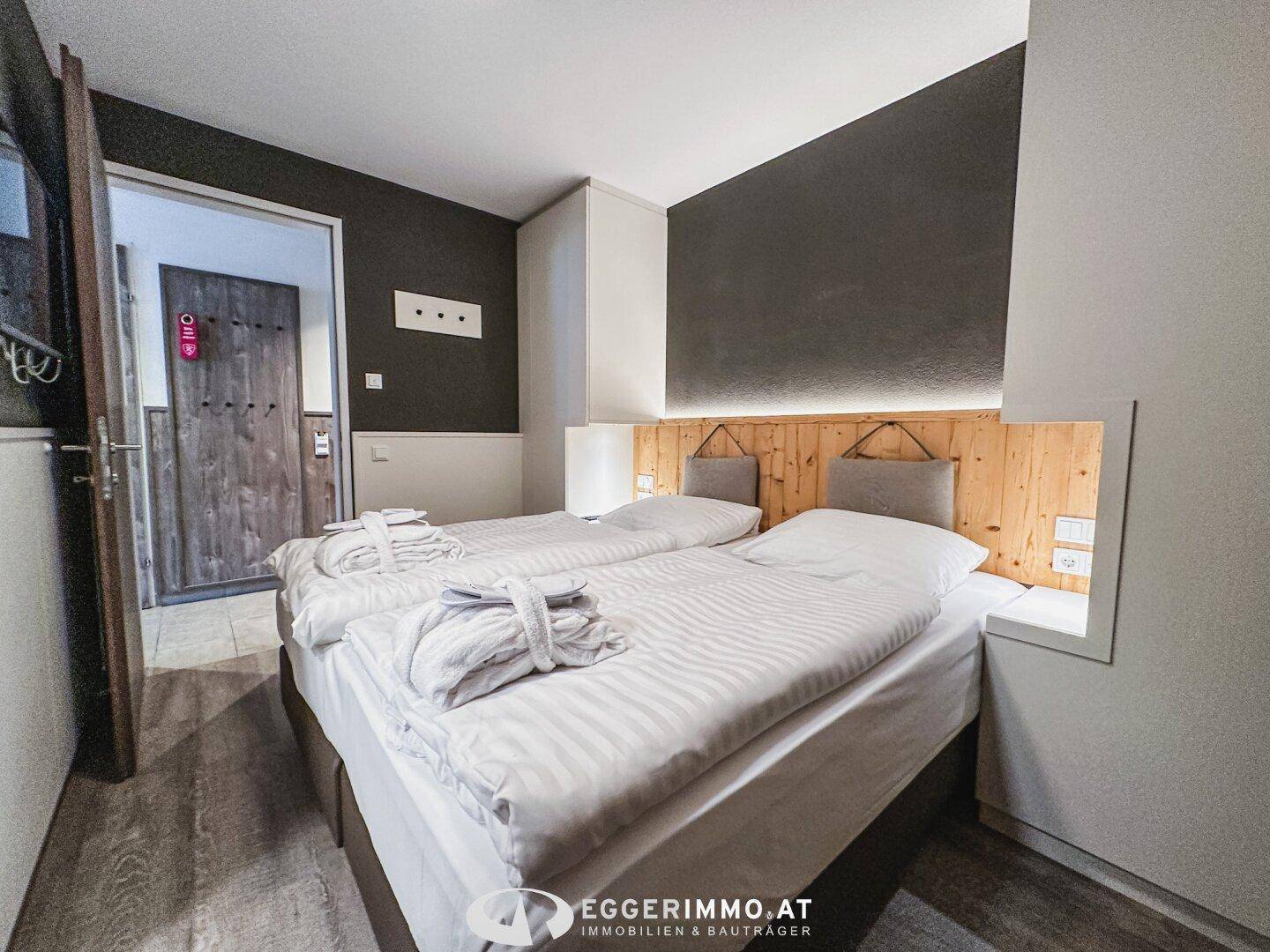 Gemütliches Schlafzimmer mit zwei Einzelbetten, Holzkopfteil und indirekter Beleuchtung.