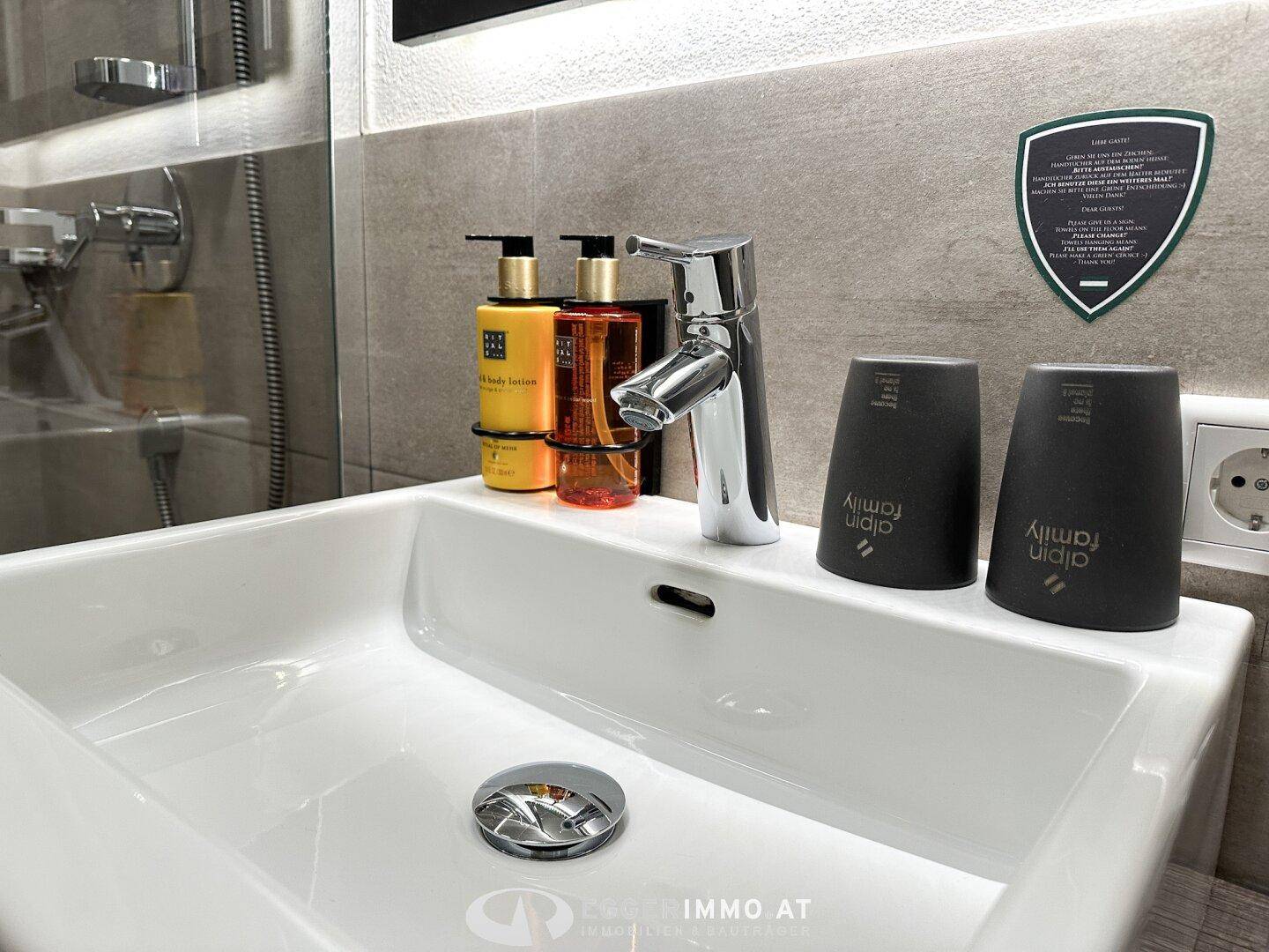 Detailaufnahme des modernen Waschbeckens mit Armatur und Pflegeprodukten im Badezimmer.