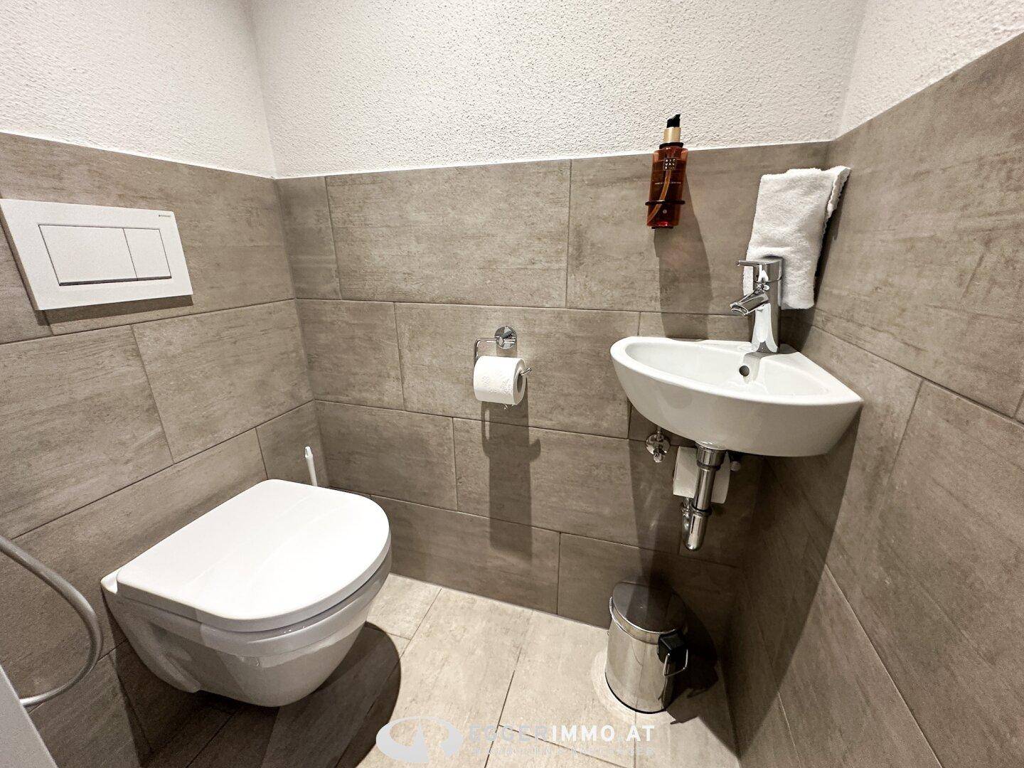 Kleines Gäste-WC mit Wand-WC, Handwaschbecken und modernen Fliesen.