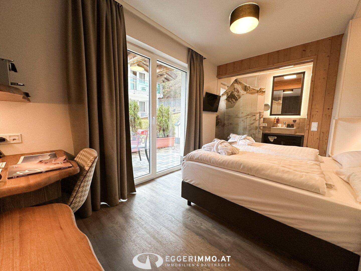Helles Schlafzimmer mit Doppelbett, Schreibtisch und Zugang zu einer kleinen Terrasse.
