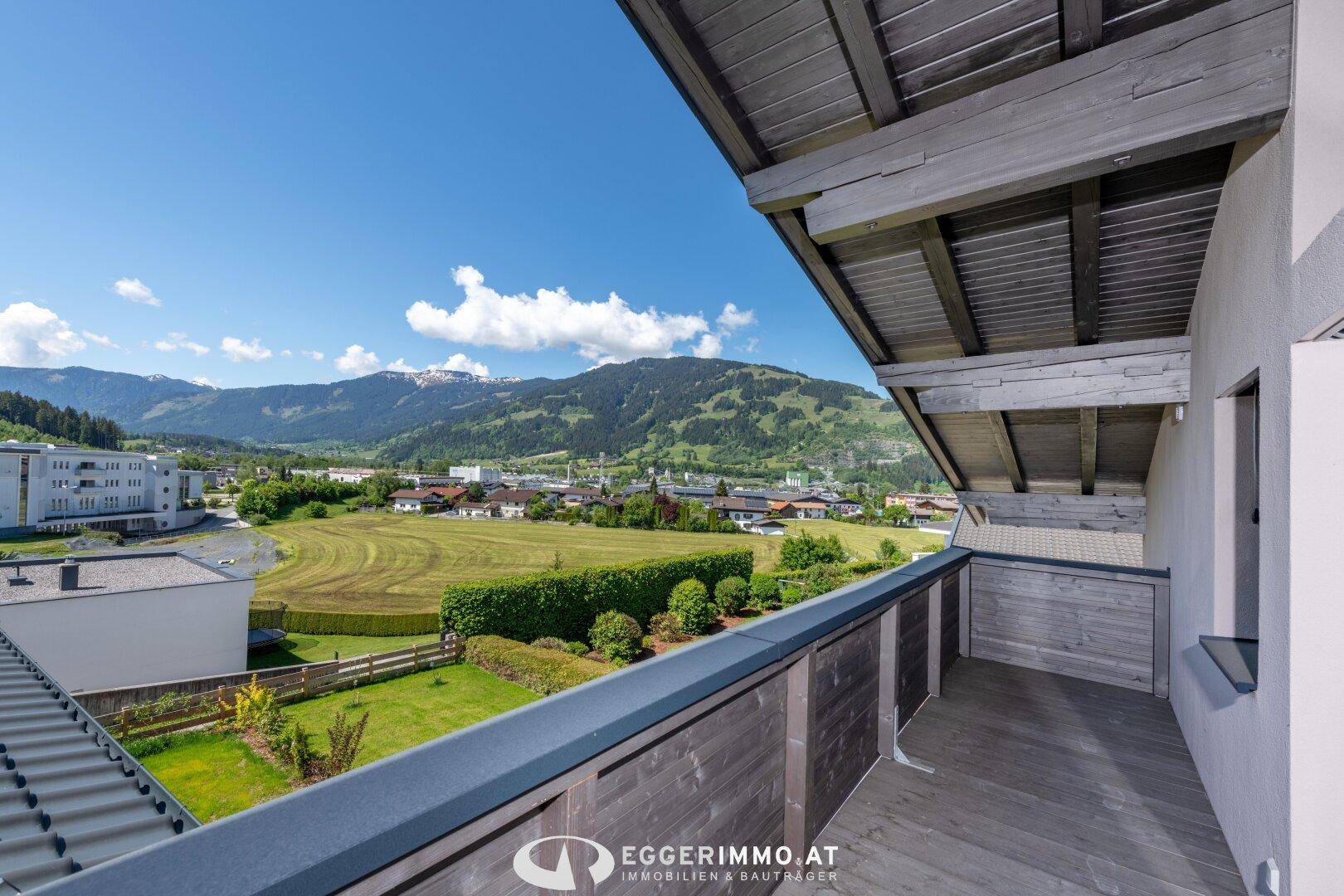 Geräumiger Balkon mit Holzboden und weitem Blick über grüne Felder und Berge.