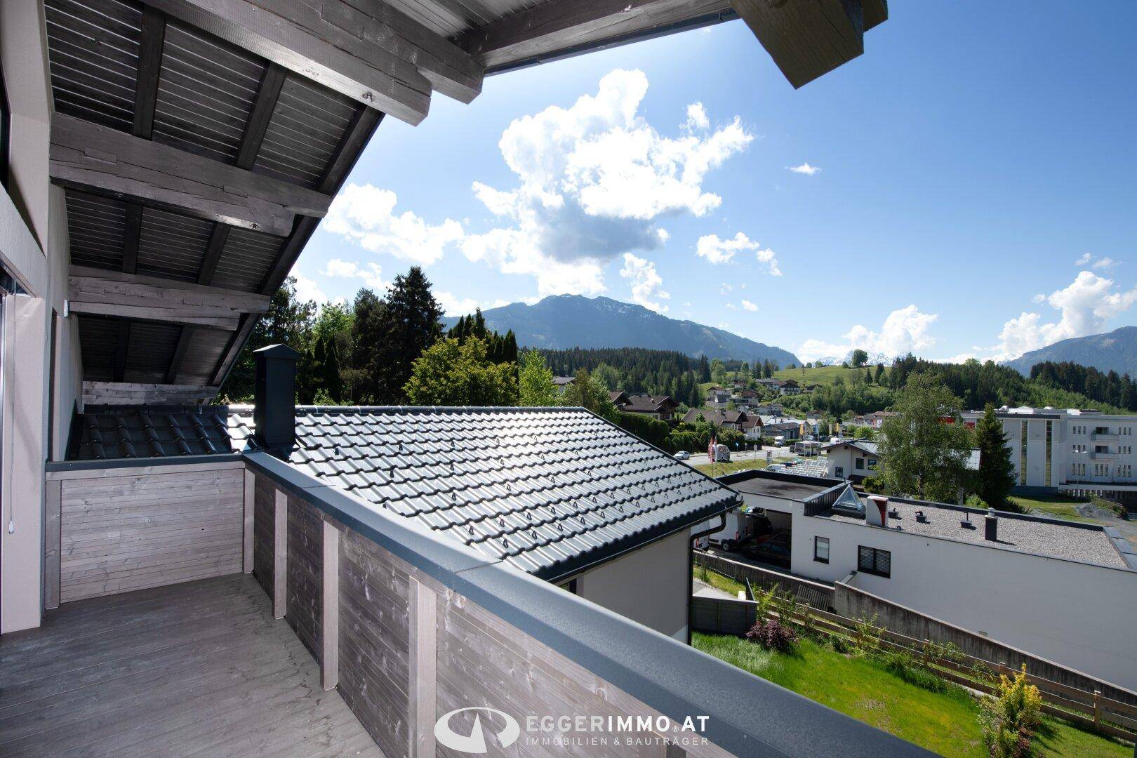 Balkon mit Holzboden und schöner Aussicht auf die umliegende Berglandschaft und Dächer.