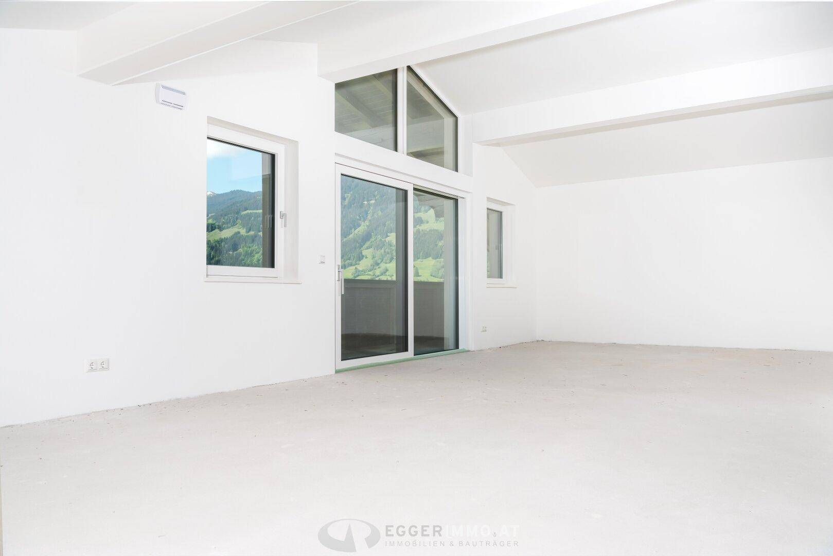 Lichtdurchfluteter Raum im Obergeschoss mit schrägen Decken und Panoramablick auf die Berge.