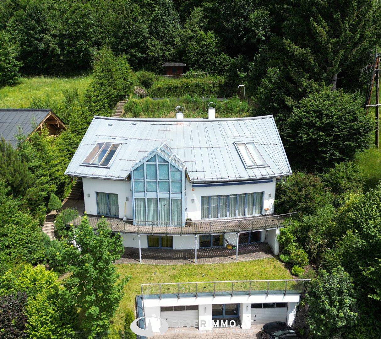 Luftaufnahme des modernen Hauses mit Garage und Balkon, umgeben von üppiger Vegetation.