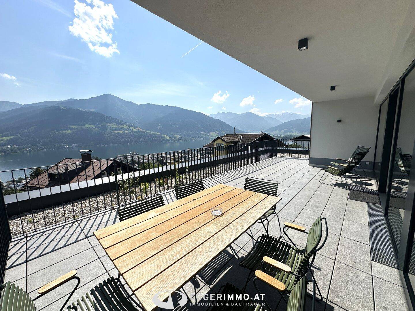 Geräumige Terrasse mit Holztisch und Stühlen, bietet einen atemberaubenden Blick auf den See und die umliegenden Berge.