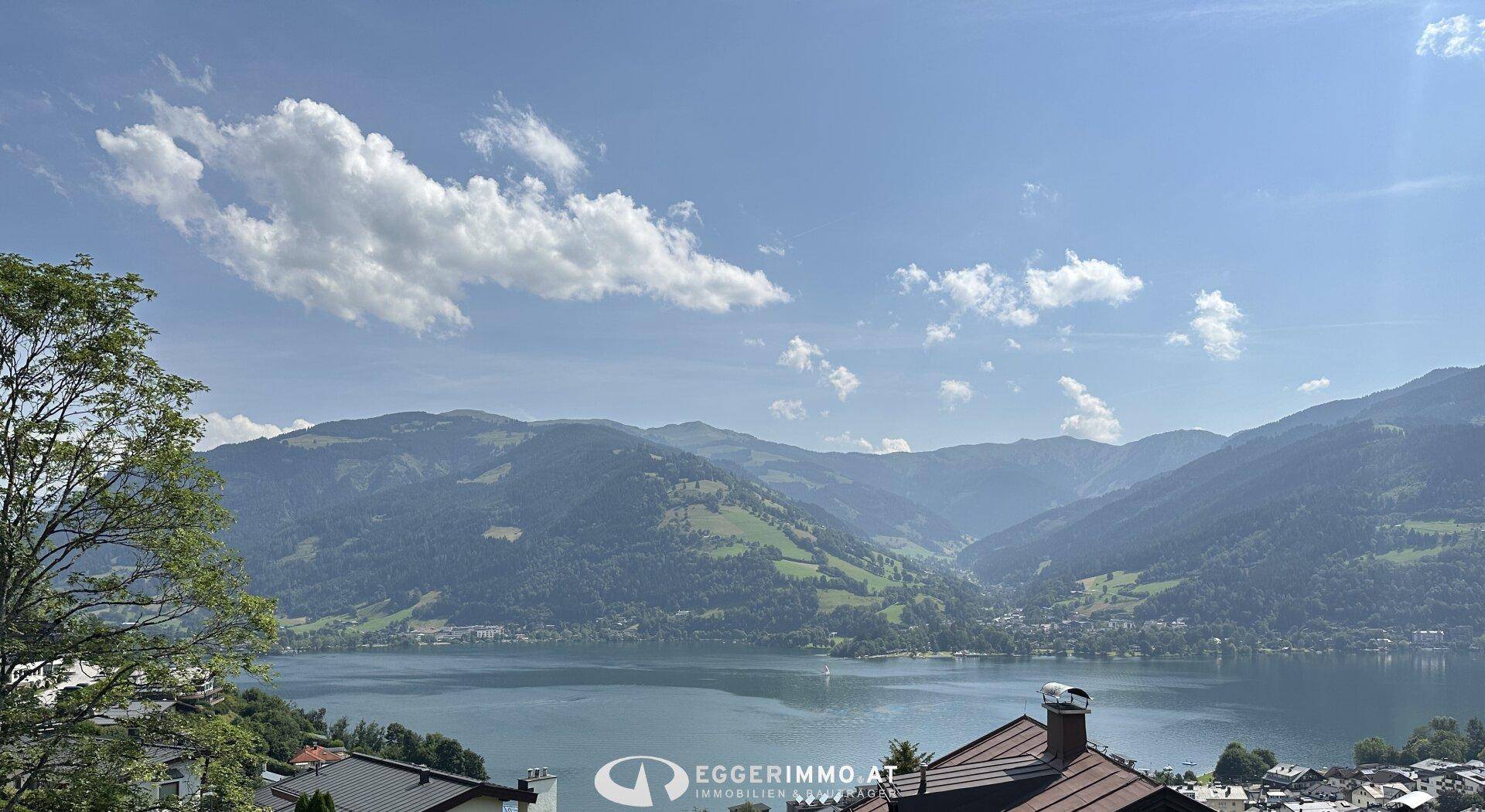 Malerischer Ausblick auf einen weitläufigen See, umgeben von grünen Bergen unter einem strahlend blauen Himmel.