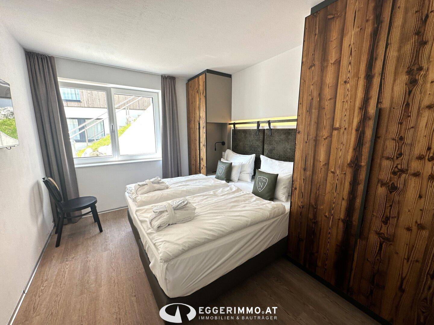 Gemütliches Schlafzimmer mit zwei Einzelbetten, Holzkleiderschränken und einem Fenster mit Blick nach draußen.