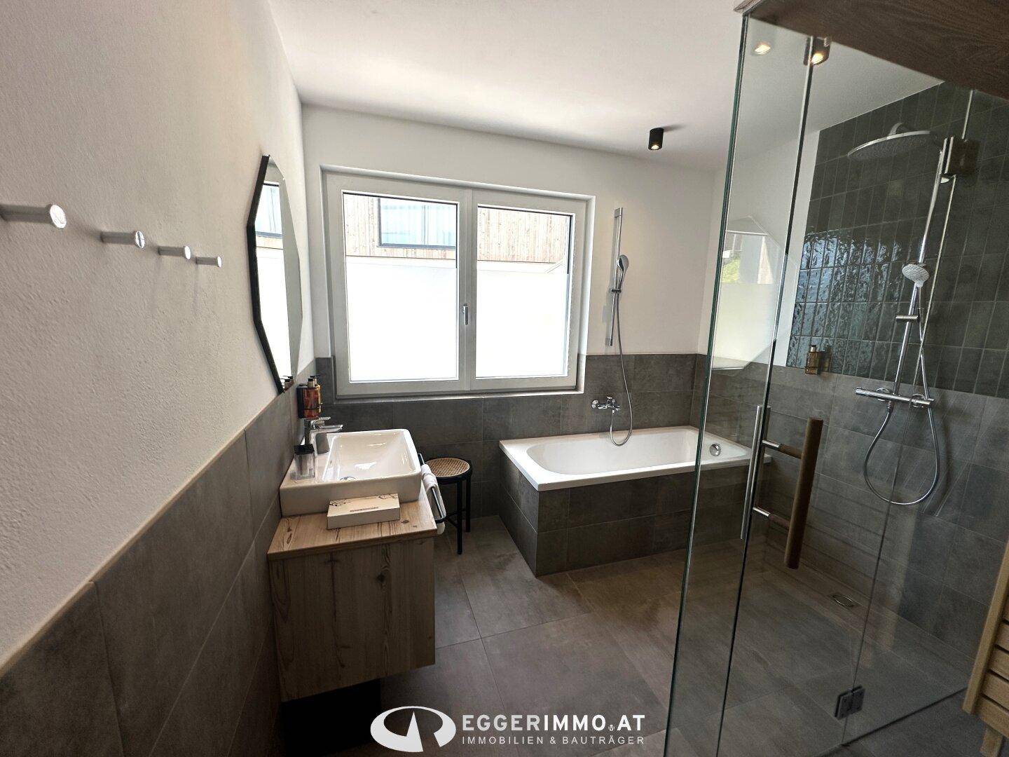 Modernes Badezimmer mit Waschtisch, Badewanne und begehbarer Dusche, durch ein Fenster hell beleuchtet.