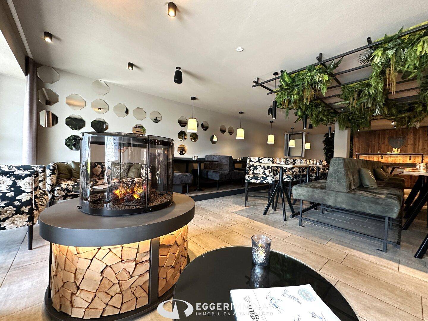 Gemütlicher Restaurant- oder Loungebereich mit einem runden Kamin, vielfältigen Sitzgelegenheiten und hängenden Pflanzen.