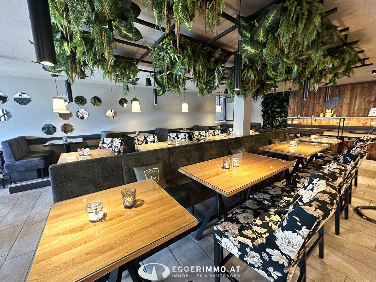Einladender Restaurantbereich mit Holztischen, bequemen Sitzbänken und dekorativen Hängepflanzen.