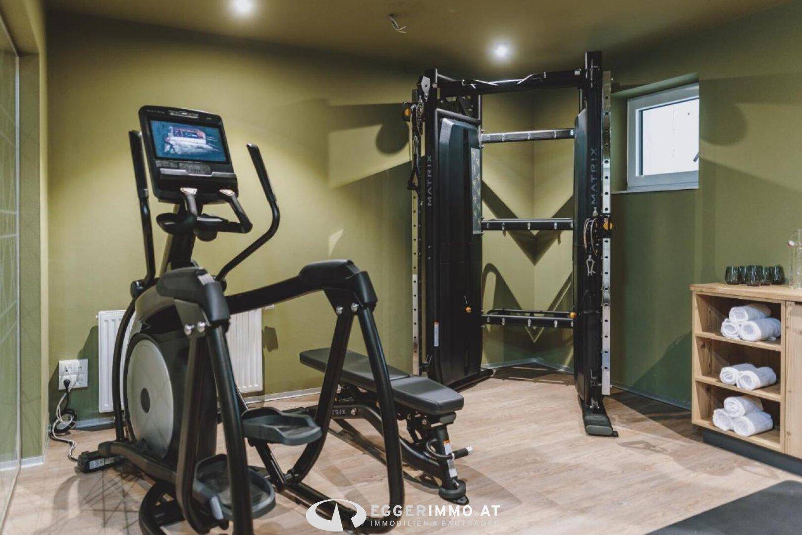 Gut ausgestatteter Fitnessraum mit modernen Trainingsgeräten und einem Fenster für natürliches Licht.