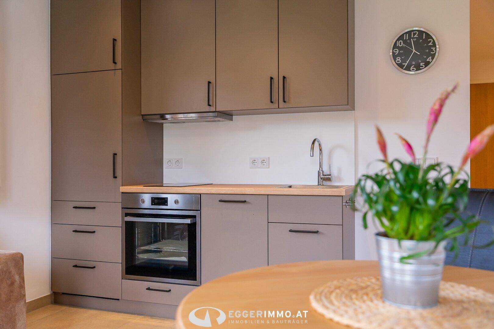 Moderne Küchenzeile mit integriertem Backofen, Spüle und Holz-Arbeitsplatte.