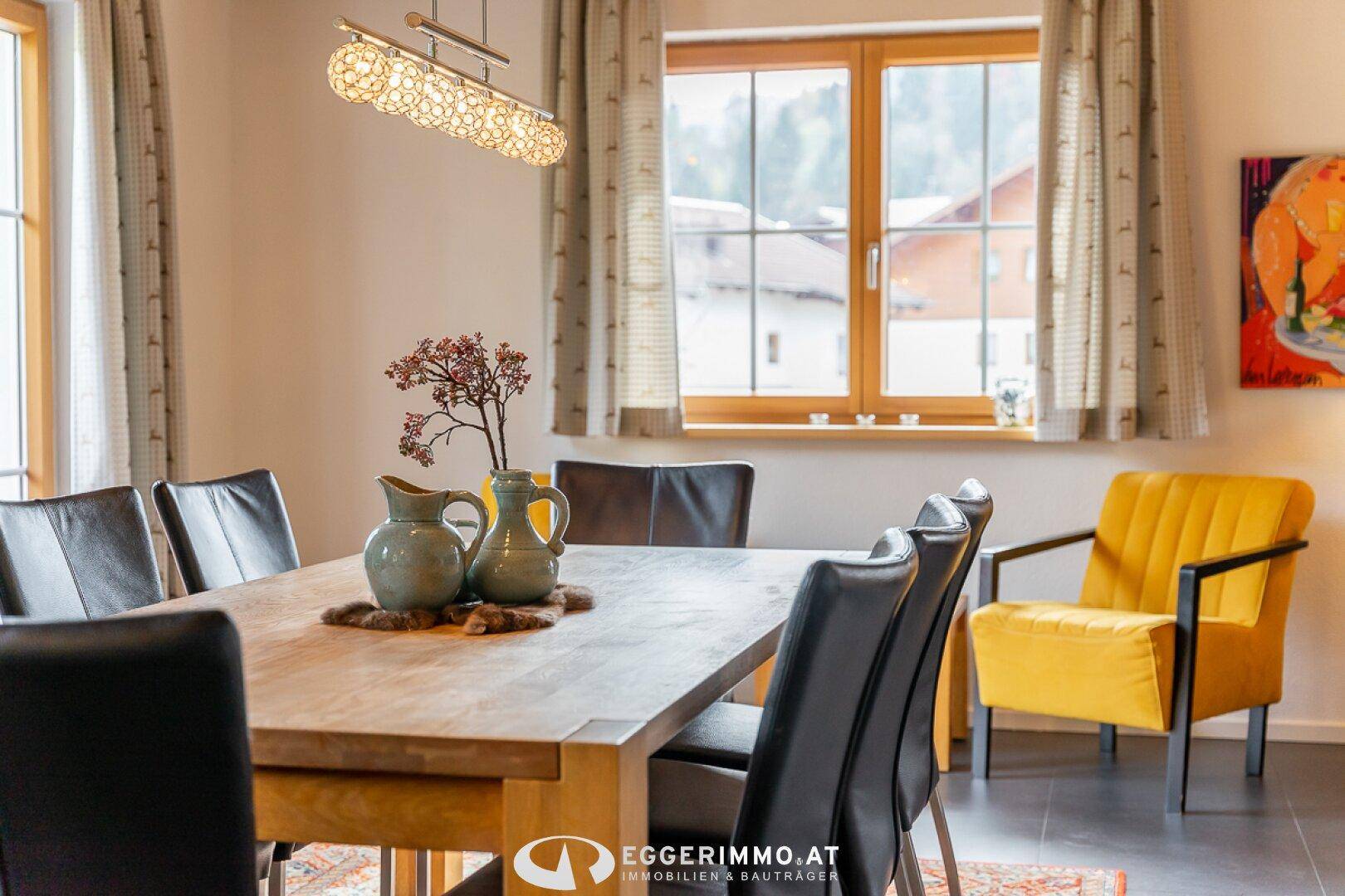 Eleganter Essbereich mit großem Holztisch, schwarzen Stühlen und gelbem Sessel.