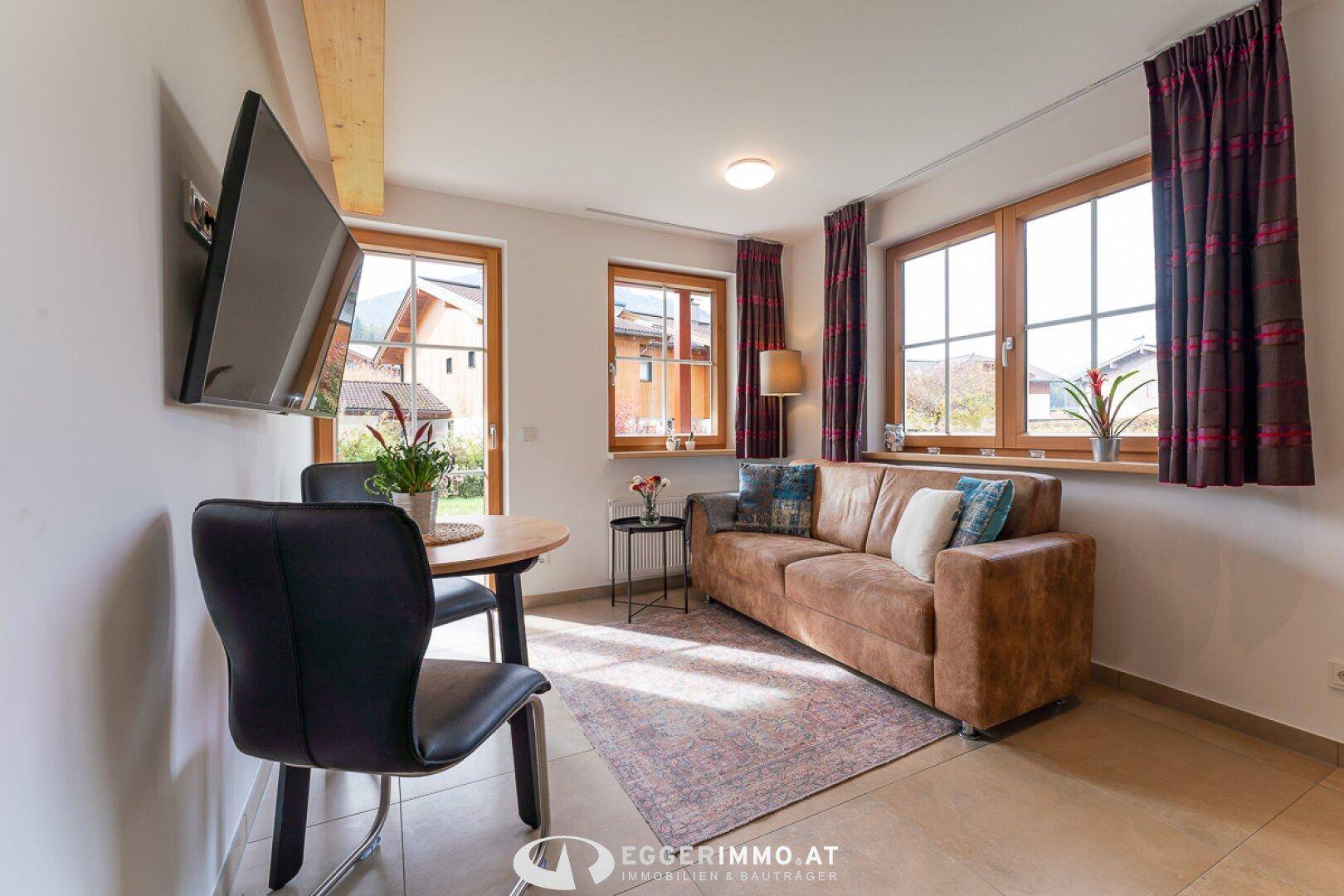 Heller Wohn- und Essbereich mit braunem Sofa, Esstisch und Blick nach draußen.