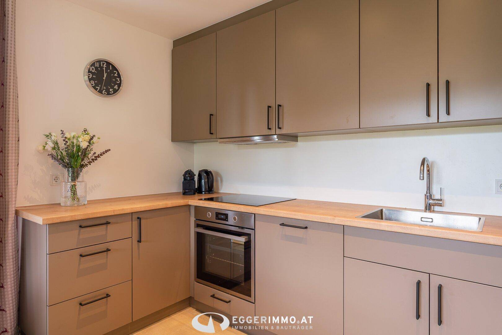 Moderne Küche mit grauen Schränken, Holz-Arbeitsplatte und integrierten Geräten.