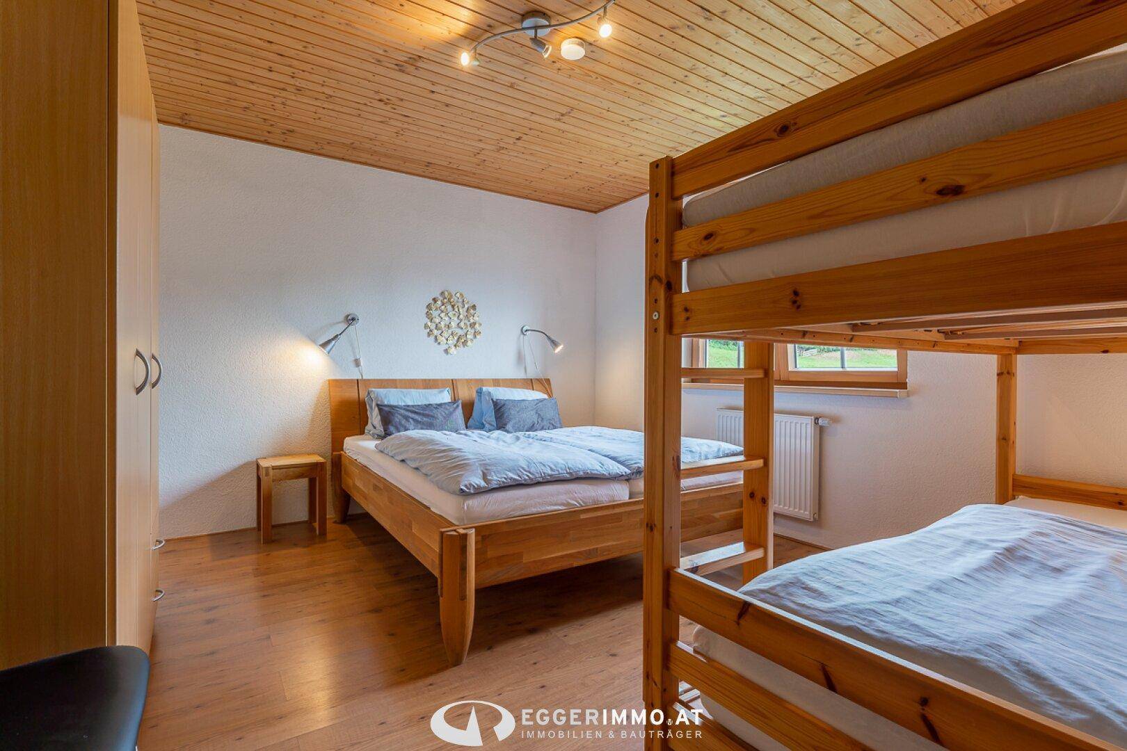 Gemütliches Schlafzimmer mit Doppelbett, Etagenbett und Holzdecke.