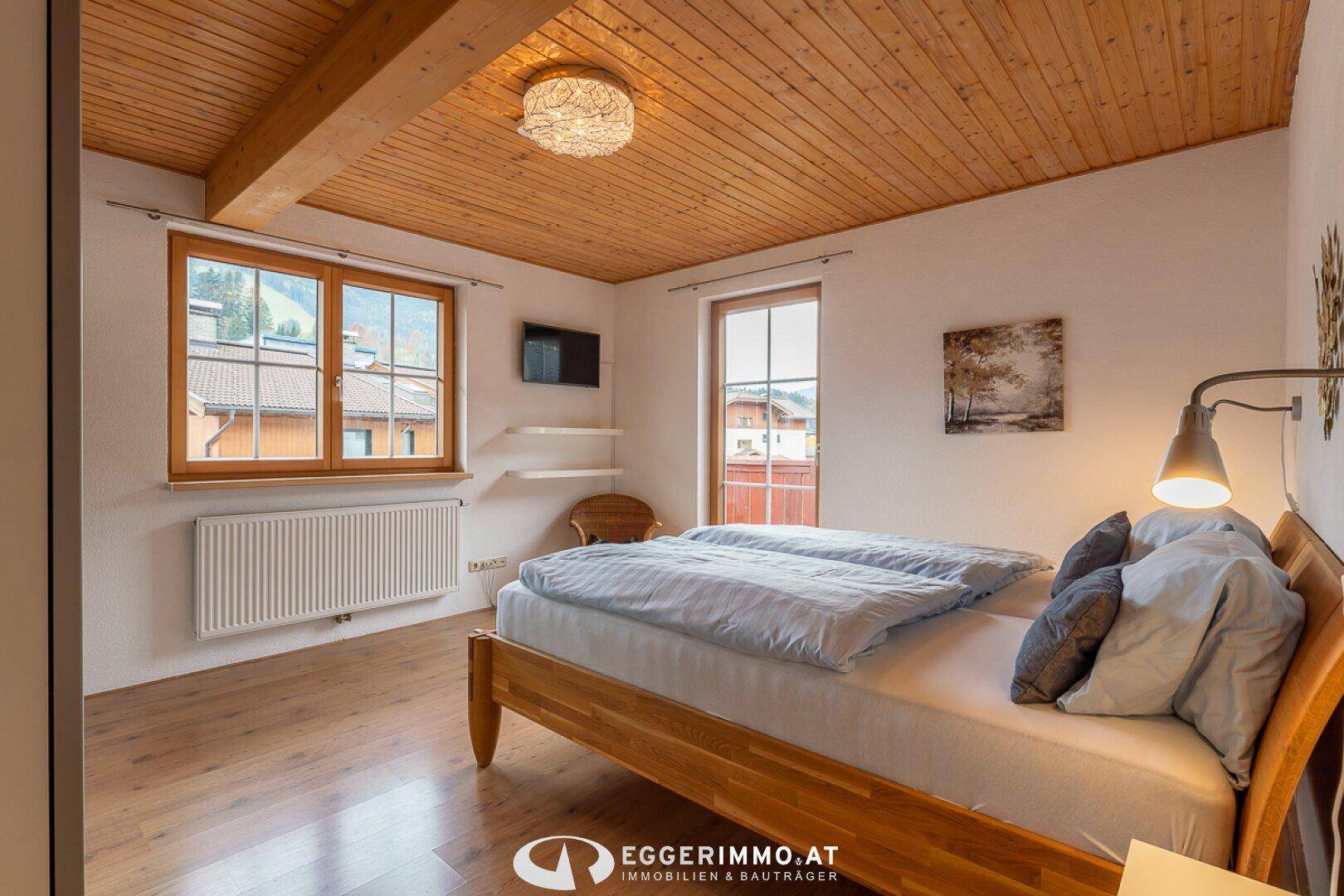 Helles Schlafzimmer mit Doppelbett, Holzdecke und Fenstern mit Ausblick.