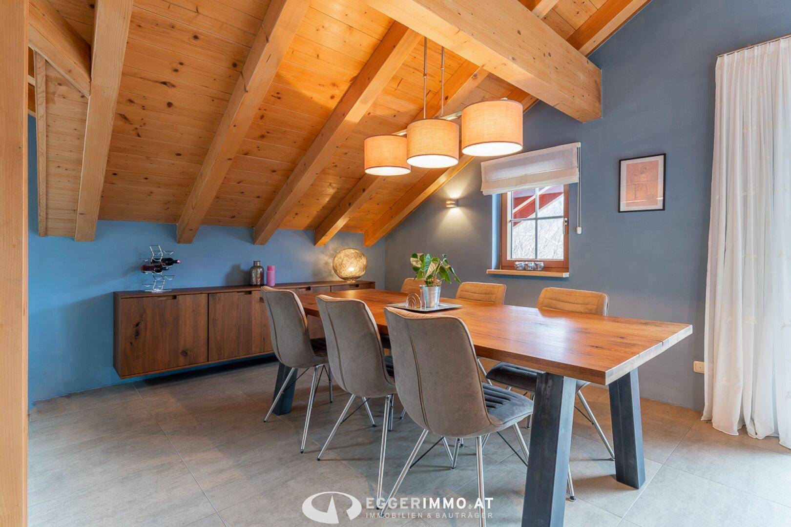 Essbereich mit Holztisch, modernen Stühlen und einem Sideboard unter einer beeindruckenden Holzbalkendecke.