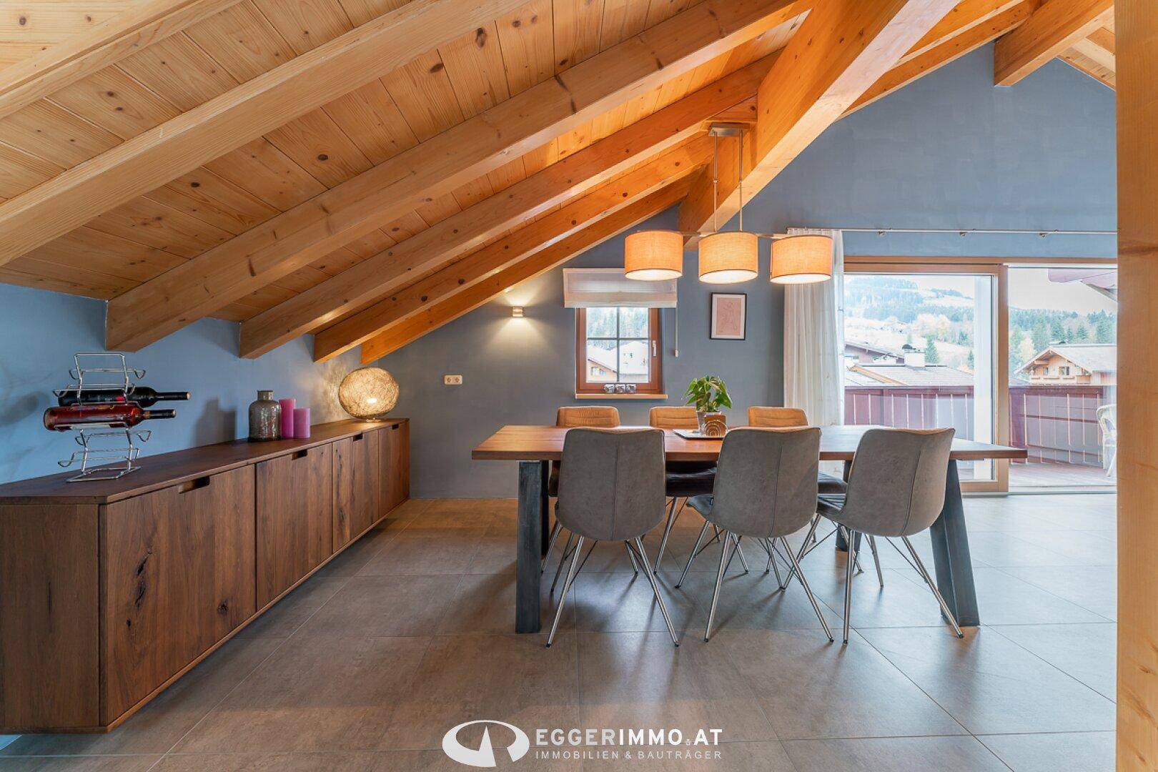 Heller Essbereich mit Holztisch, Sideboard und Zugang zum Balkon, umgeben von einer Holzbalkendecke.