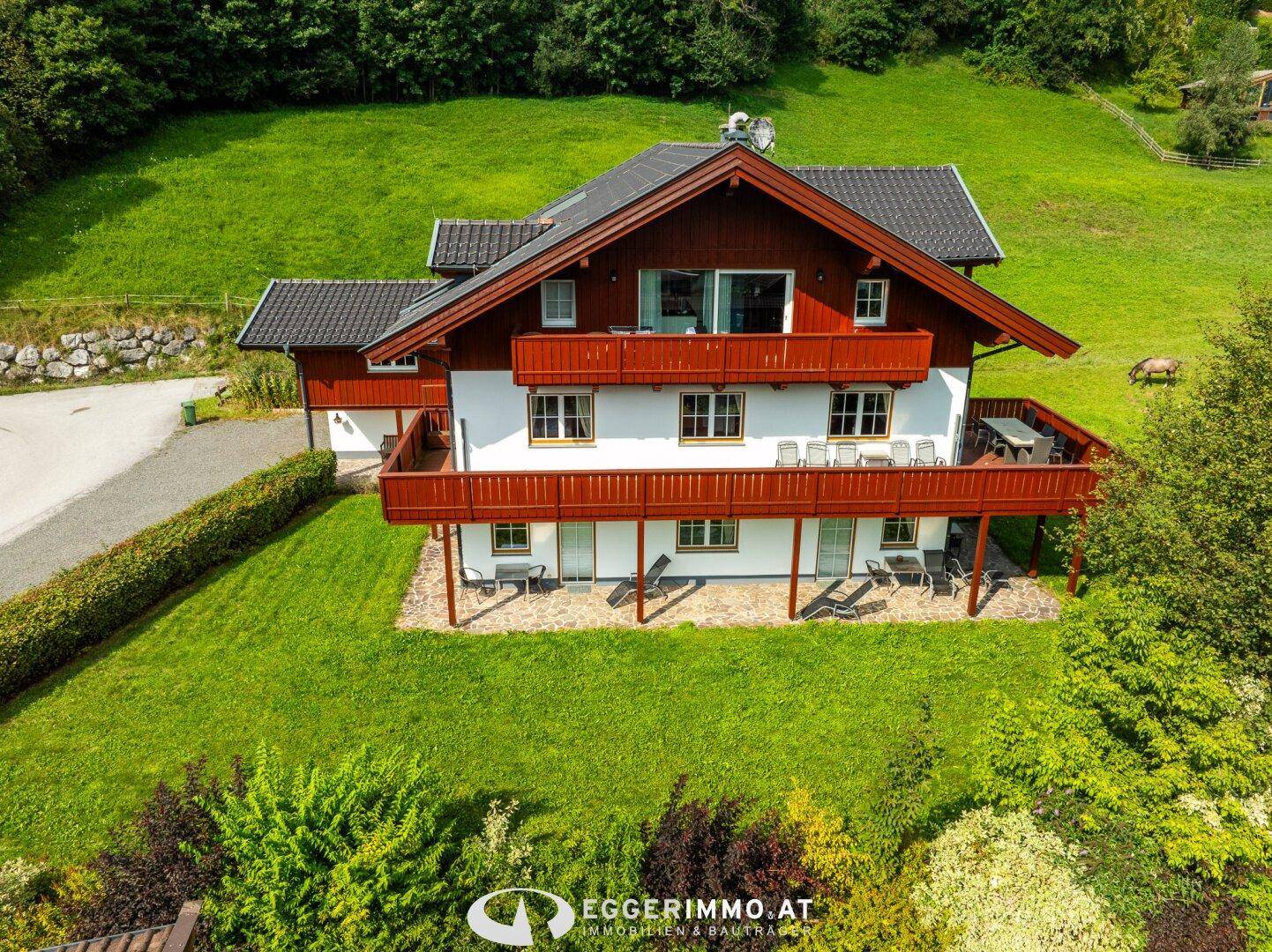 Charmantes Landhaus mit mehreren Balkonen und Terrassen, eingebettet in grüne Hügellandschaft.