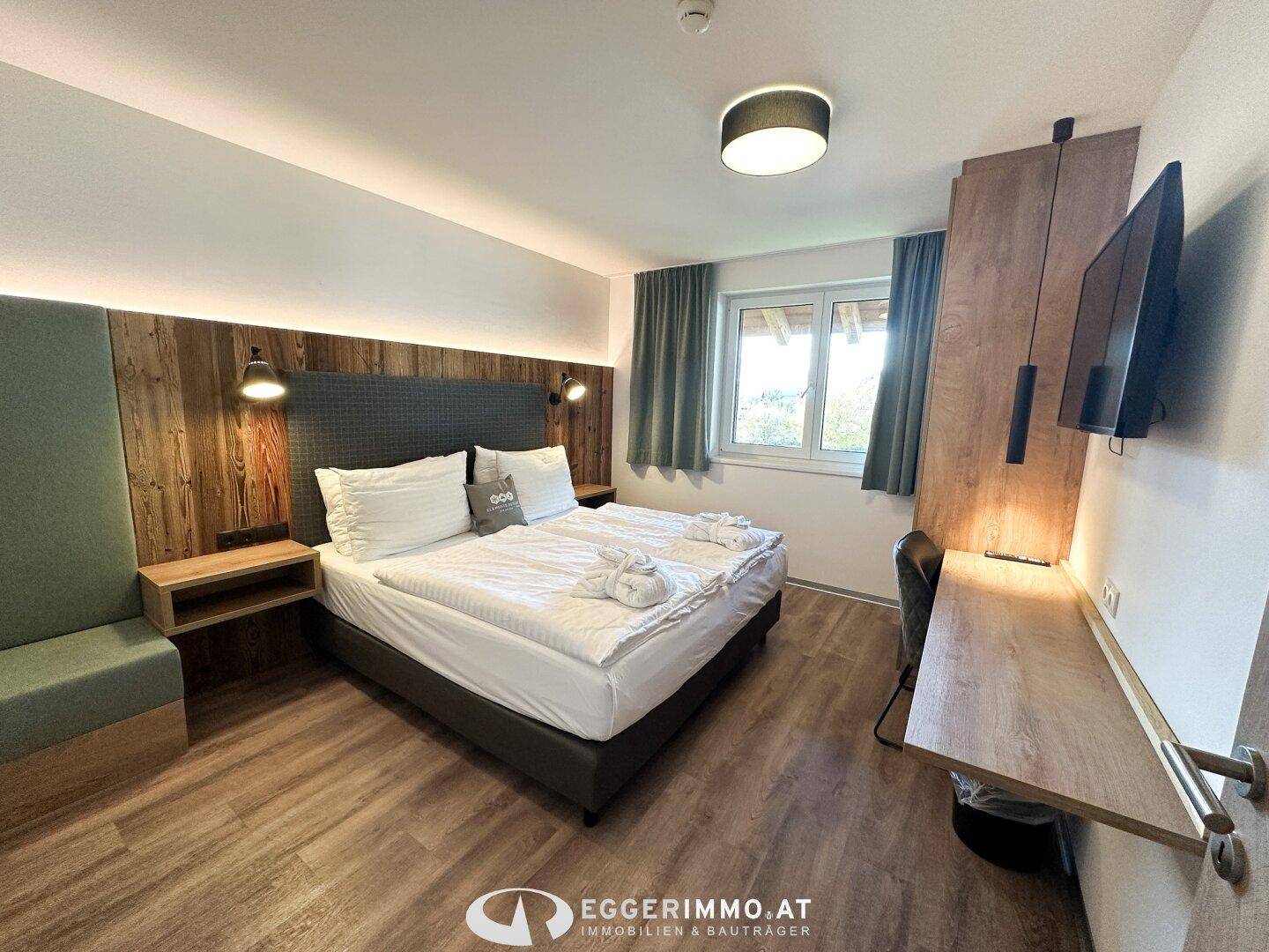 Helles Schlafzimmer mit Doppelbett, Holzwandpaneelen und Blick ins Grüne.