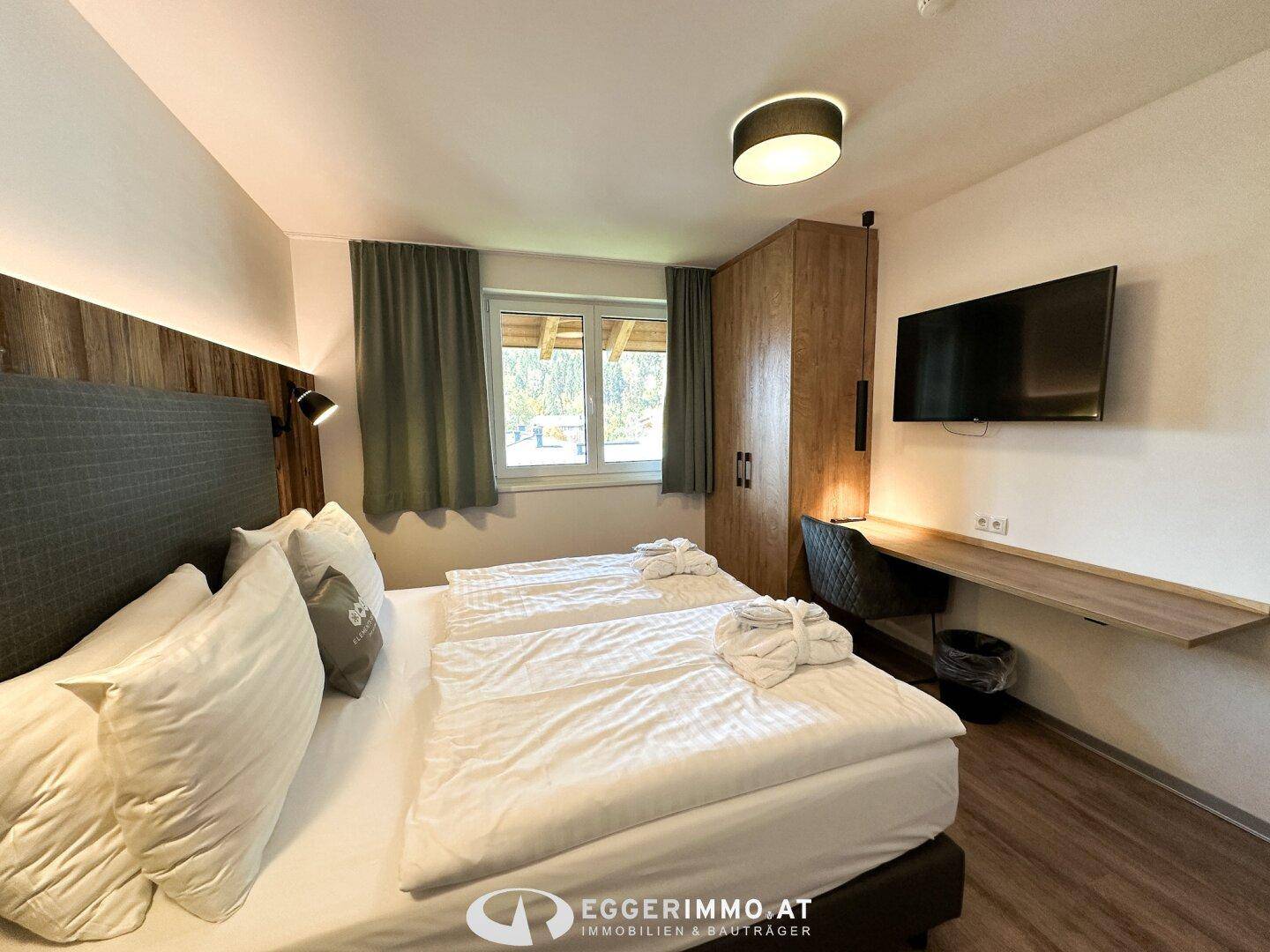 Helles Schlafzimmer mit Doppelbett, Holzschrank und Schreibtischbereich.