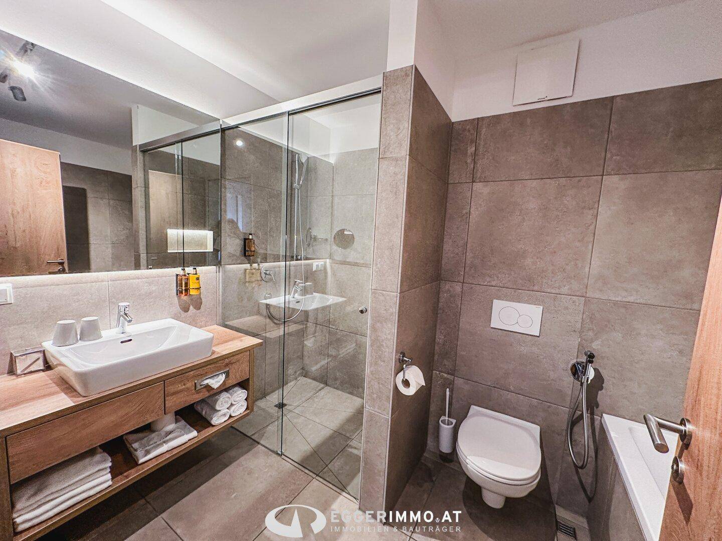 Modernes Badezimmer mit großformatigen Fliesen, begehbarer Dusche und stilvollem Waschtisch.