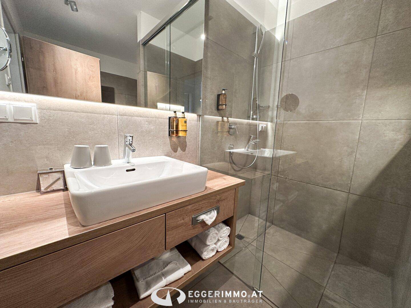 Modernes Badezimmer mit Waschtisch, großem Spiegel und begehbarer Dusche.