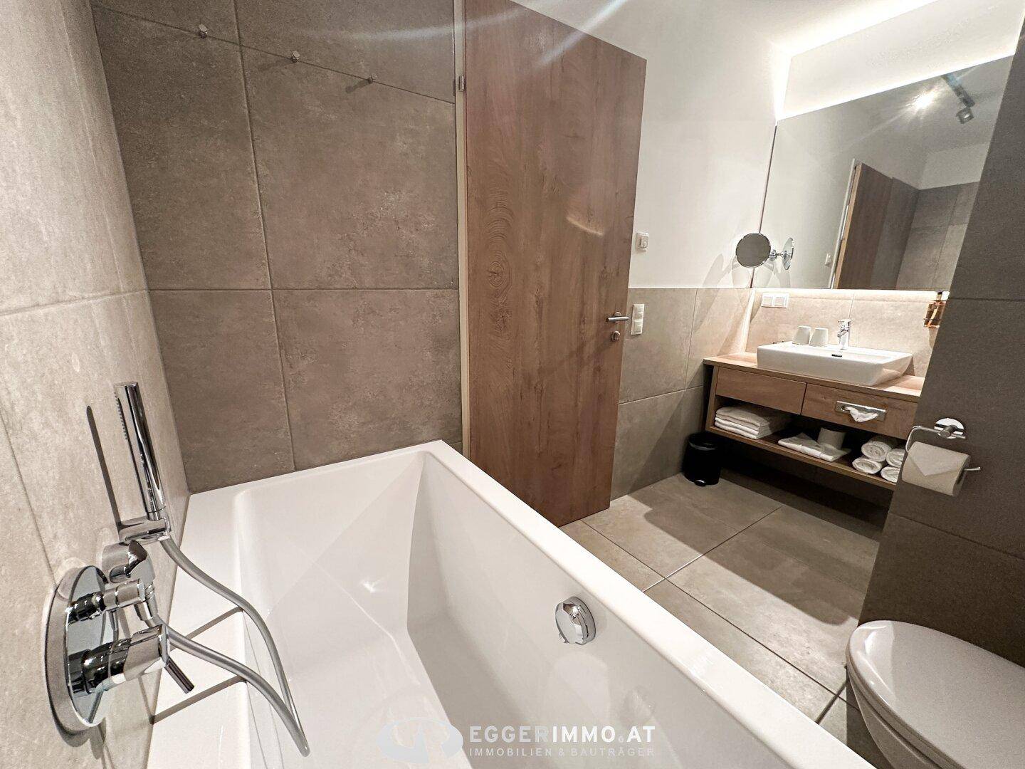Modernes Badezimmer mit Badewanne, Waschtisch und großformatigen Fliesen.