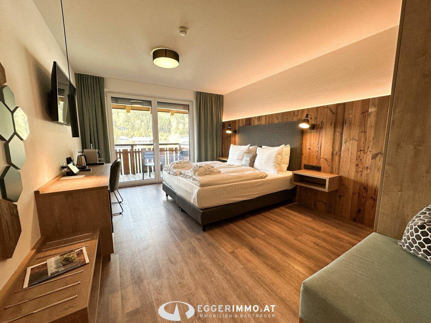 Komfortables Schlafzimmer mit Doppelbett, Holzwand und Zugang zum Balkon.